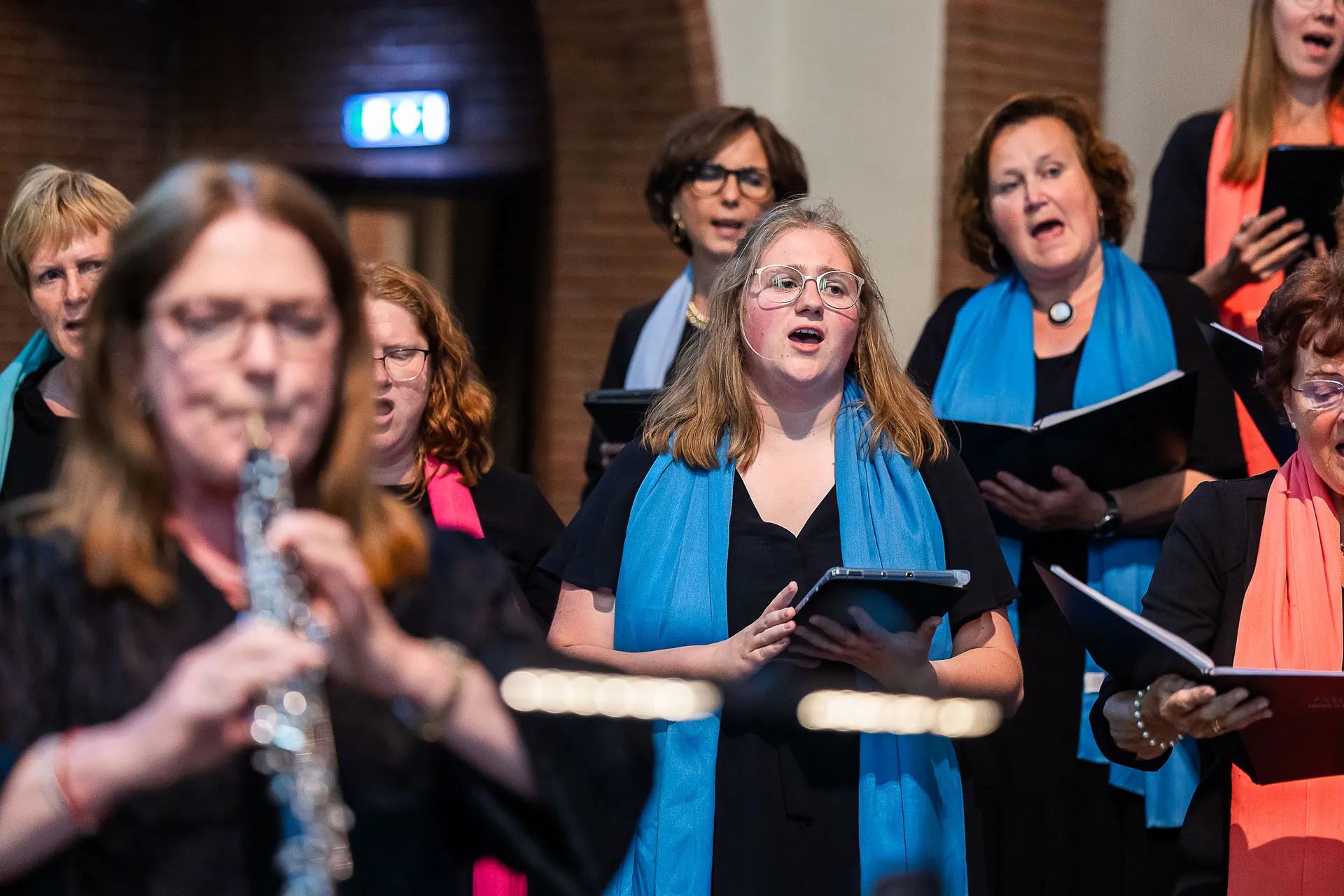 Leden van Interkerkelijk Koor Immanuël zingen in de kerk, met kleurige sjaals